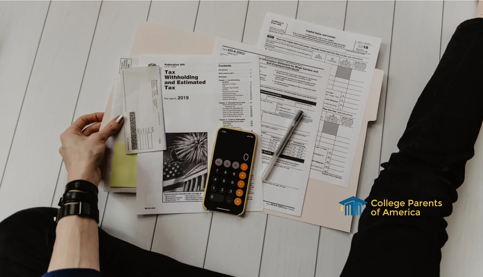 A student sits on the ground with one leg outstretched with a file folder, pen, and a phone with a calculator open