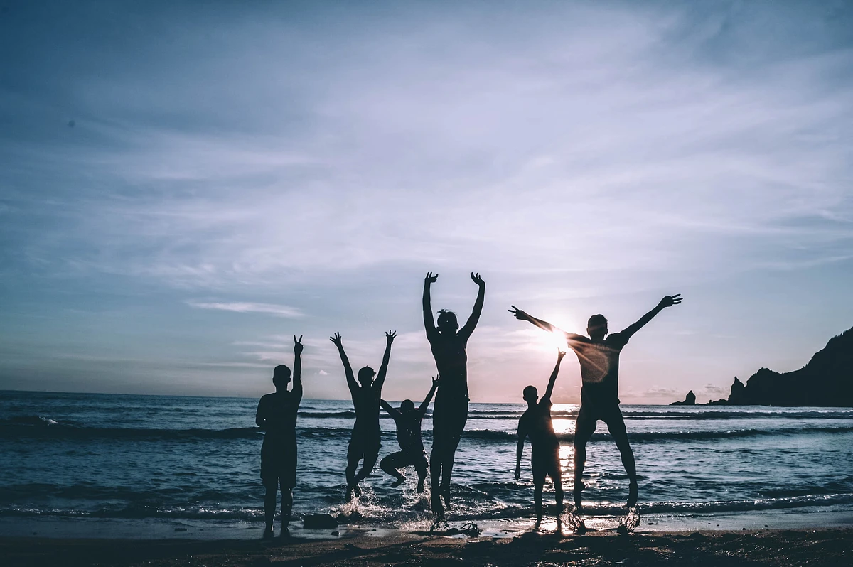 Silhouette of 6 people on beach, jumping up over the shoreline