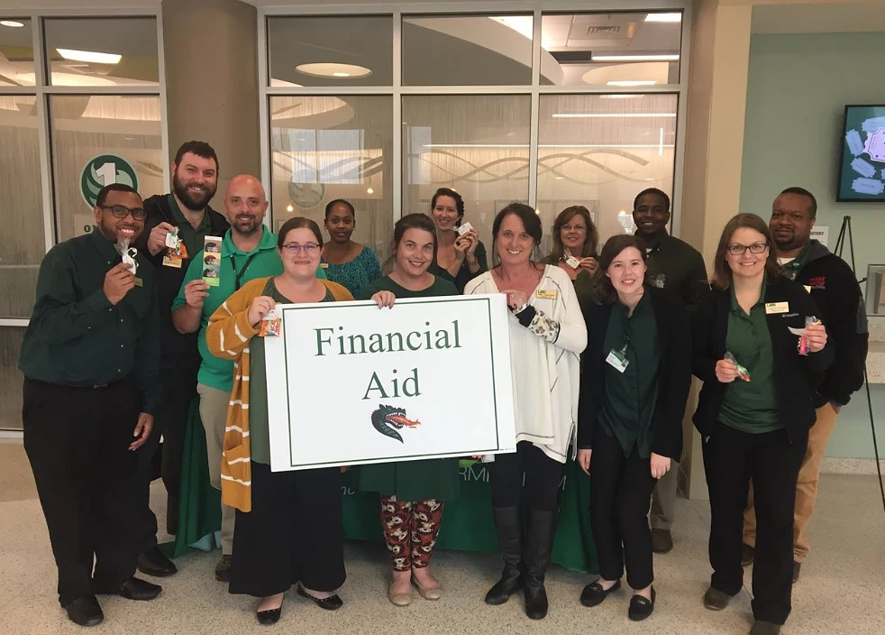 The financial staff stands together with a sign that says financial aid